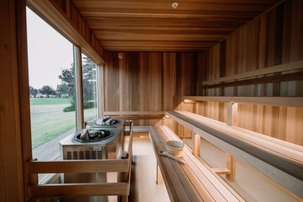 large sauna heaters surrounded by cedar, in a large sauna with benches and large window